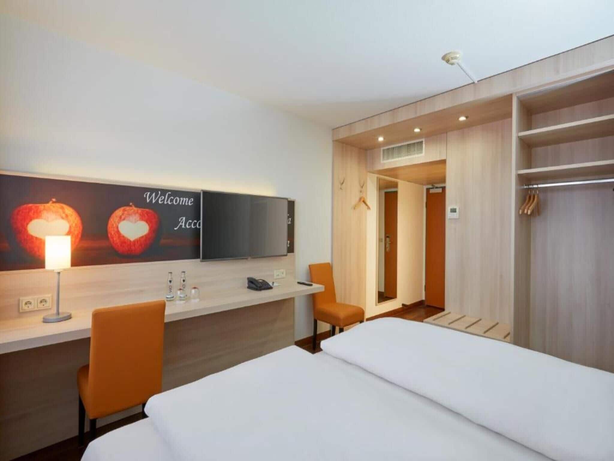 Ein Hotelzimmer mit Bett, Schreibtisch, Stuhl, Fernseher und Kleiderschrank.