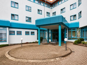 A building with a central covered area, multiple windows, and a paved courtyard with seating.