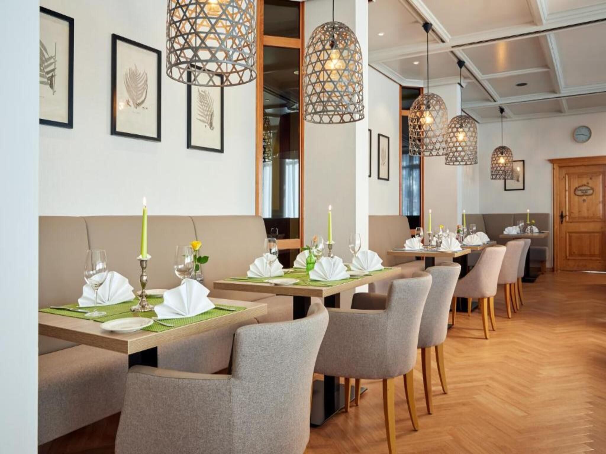 Interior de restaurante con varias mesas dispuestas para recibir comensales, iluminación colgante y obras de arte enmarcadas en las paredes.