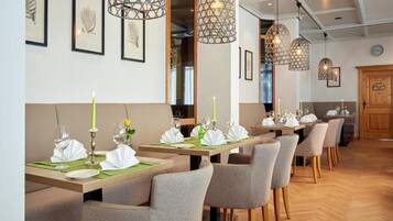 Interior de restaurante con varias mesas dispuestas para recibir comensales, iluminación colgante y obras de arte enmarcadas en las paredes.