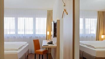 A hotel room with two beds, a desk, a chair, and a TV.