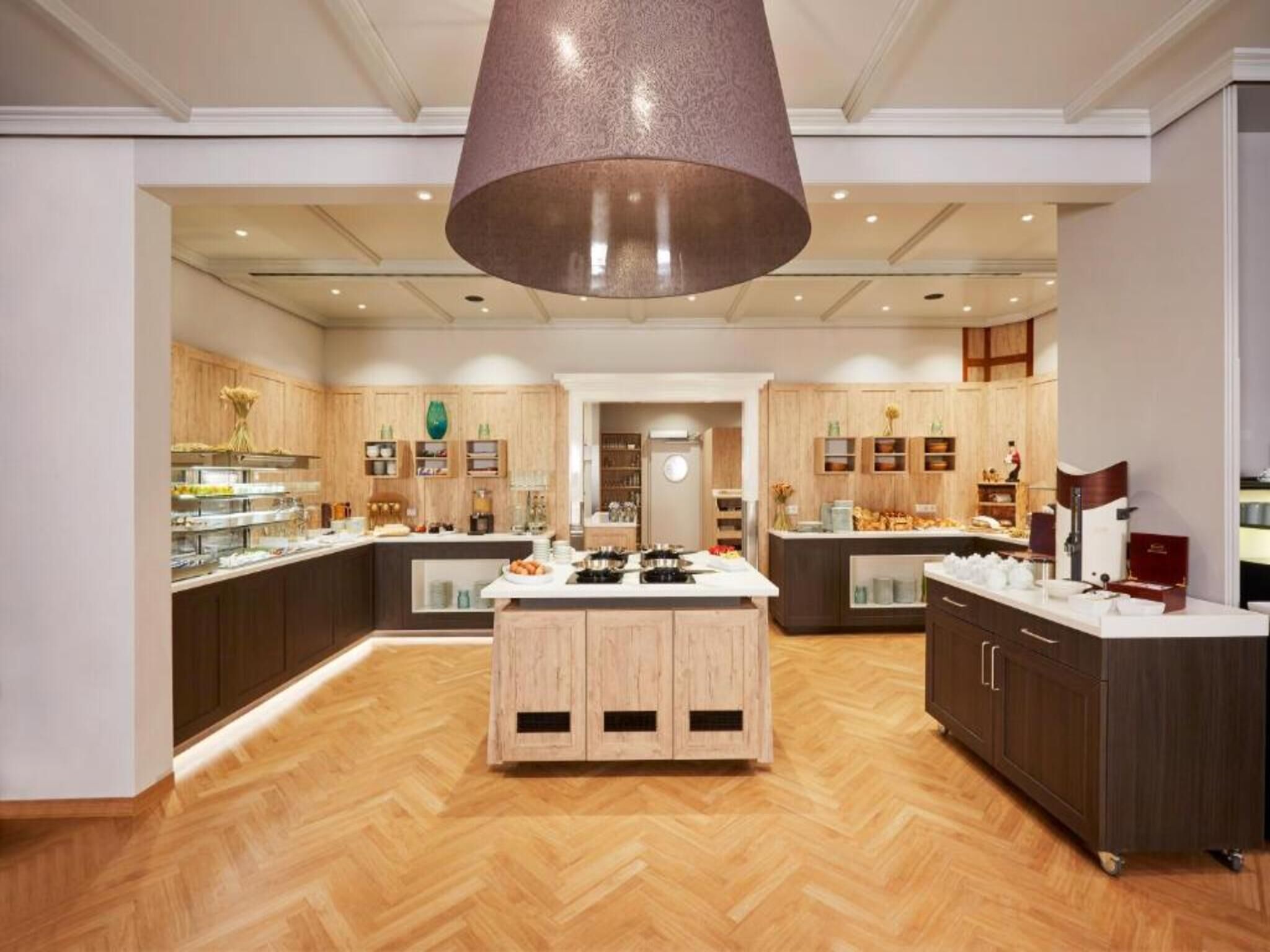 A spacious kitchen with a central island, wooden cabinets, and a large hanging light fixture.
