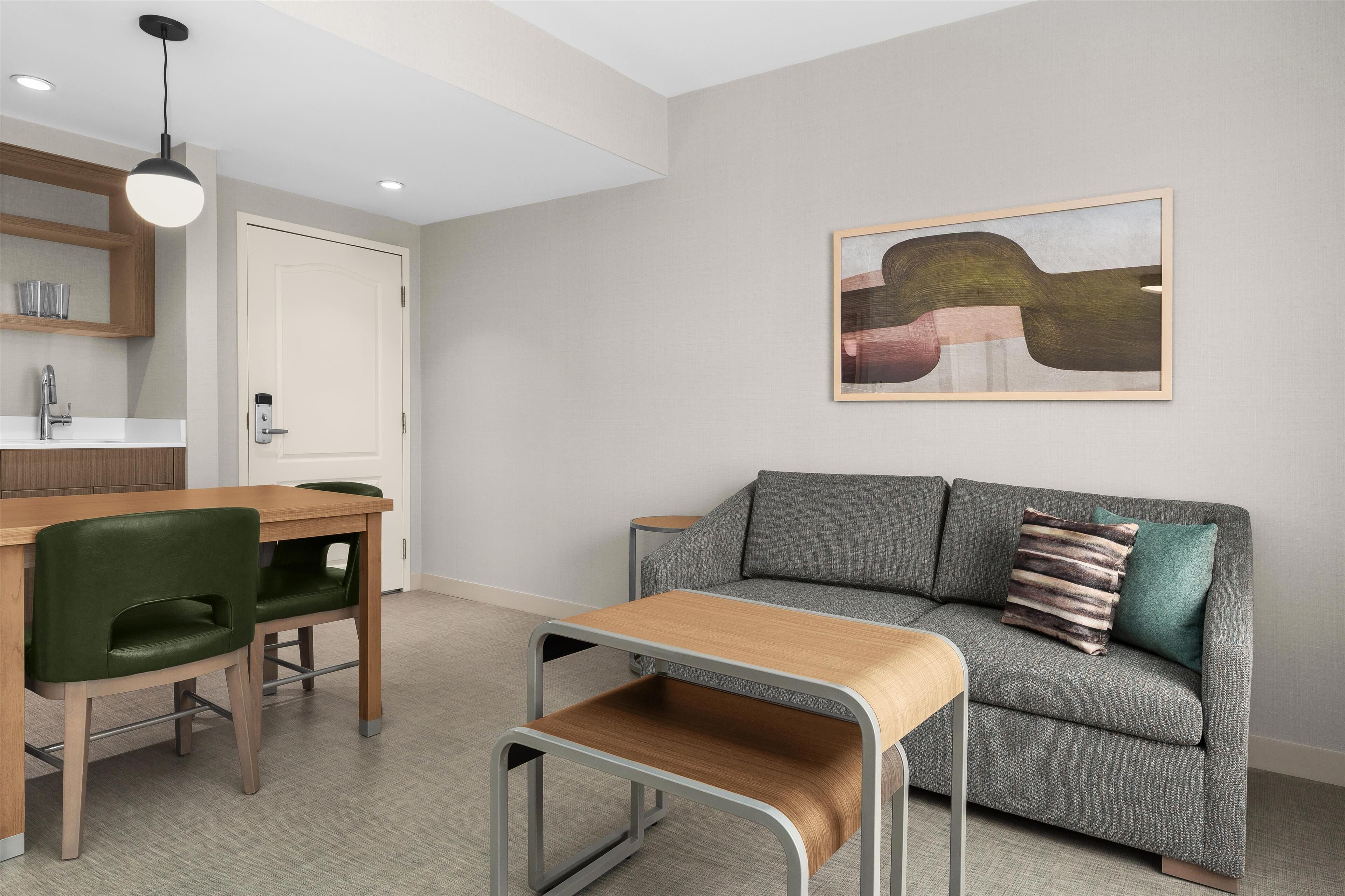 Uma sala de estar moderna com um sofá cinzento, uma mesa de centro de madeira e uma área de jantar com uma cadeira verde.