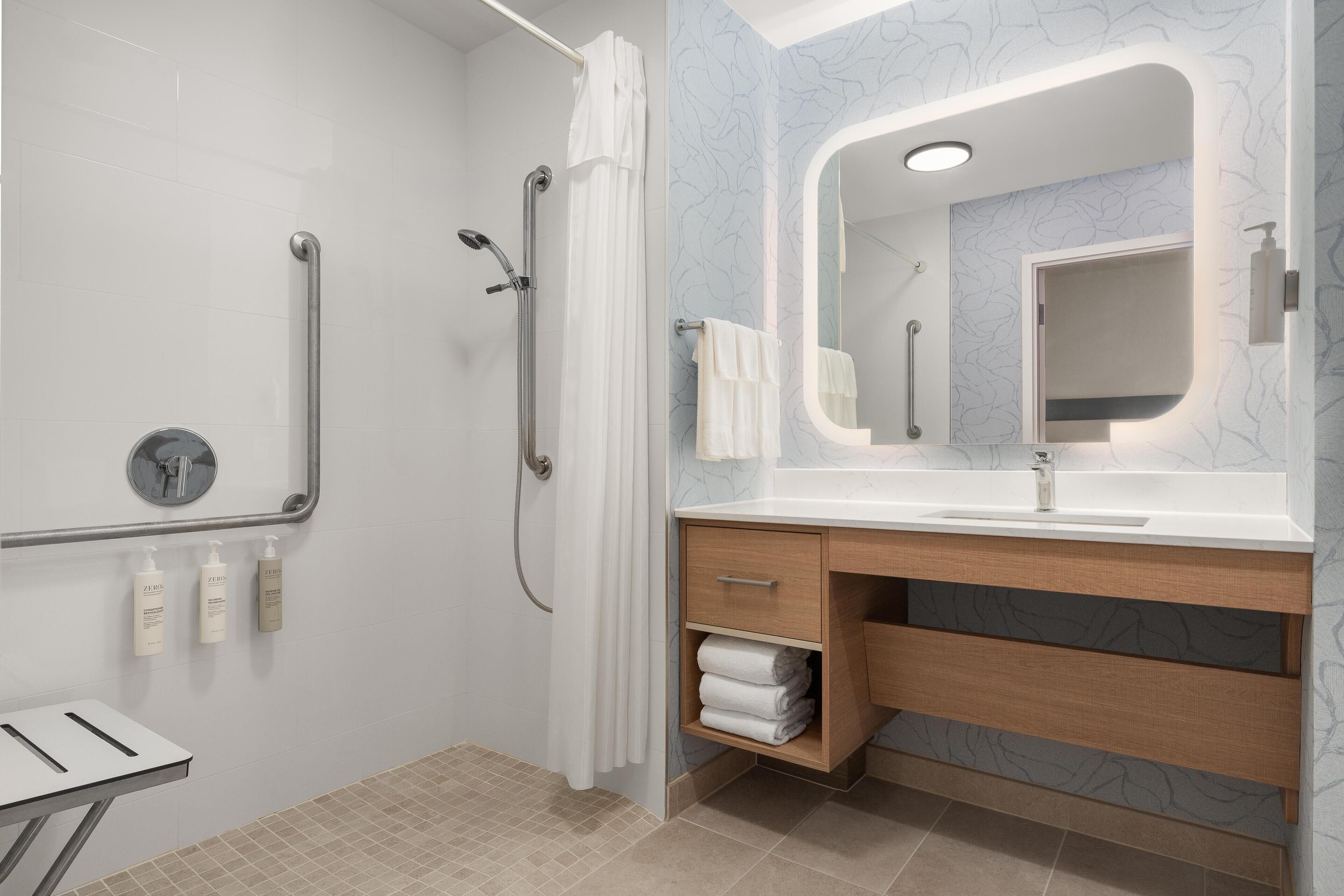 A modern bathroom with a shower, grab bars, a sink with a mirror, and a towel rack.