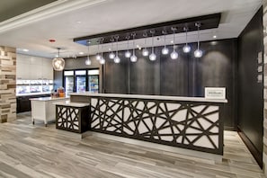Un espace d’accueil moderne, avec un comptoir de réception en bois foncé, un plan de travail blanc et un luminaire suspendu en verre.