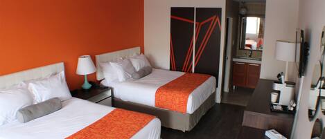 A hotel room with two beds, a desk, a mirror, and a wardrobe.