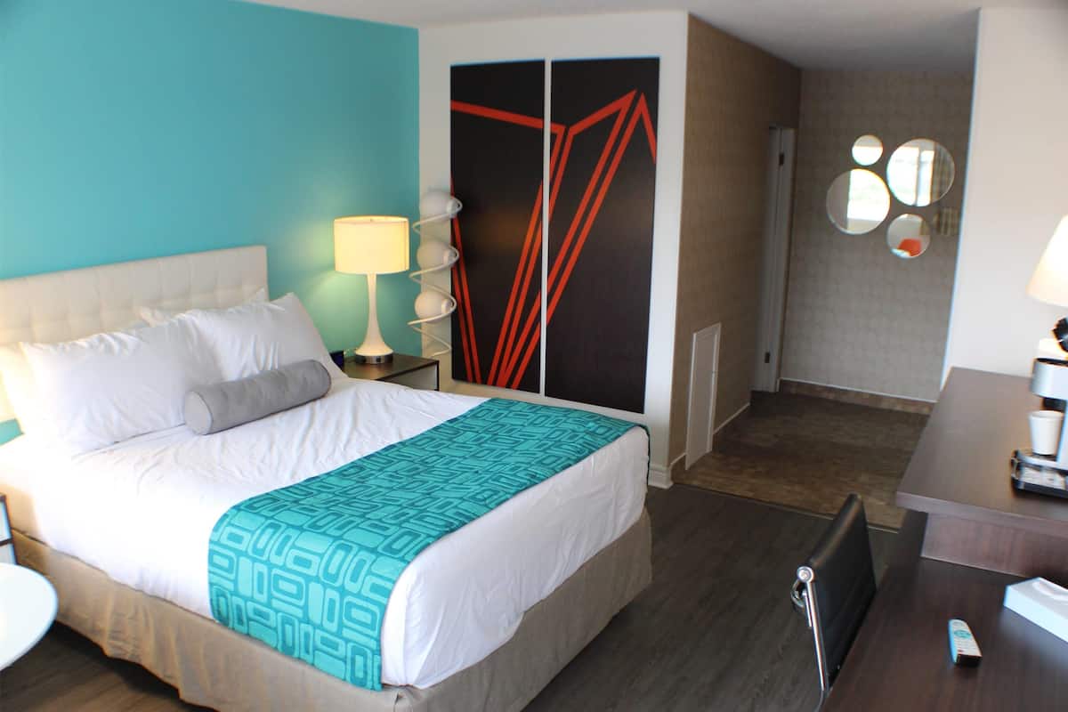 Une chambre d’hôtel équipée d’un lit, d’un bureau, d’une chaise, d’une lampe, d’une armoire et d’un miroir.