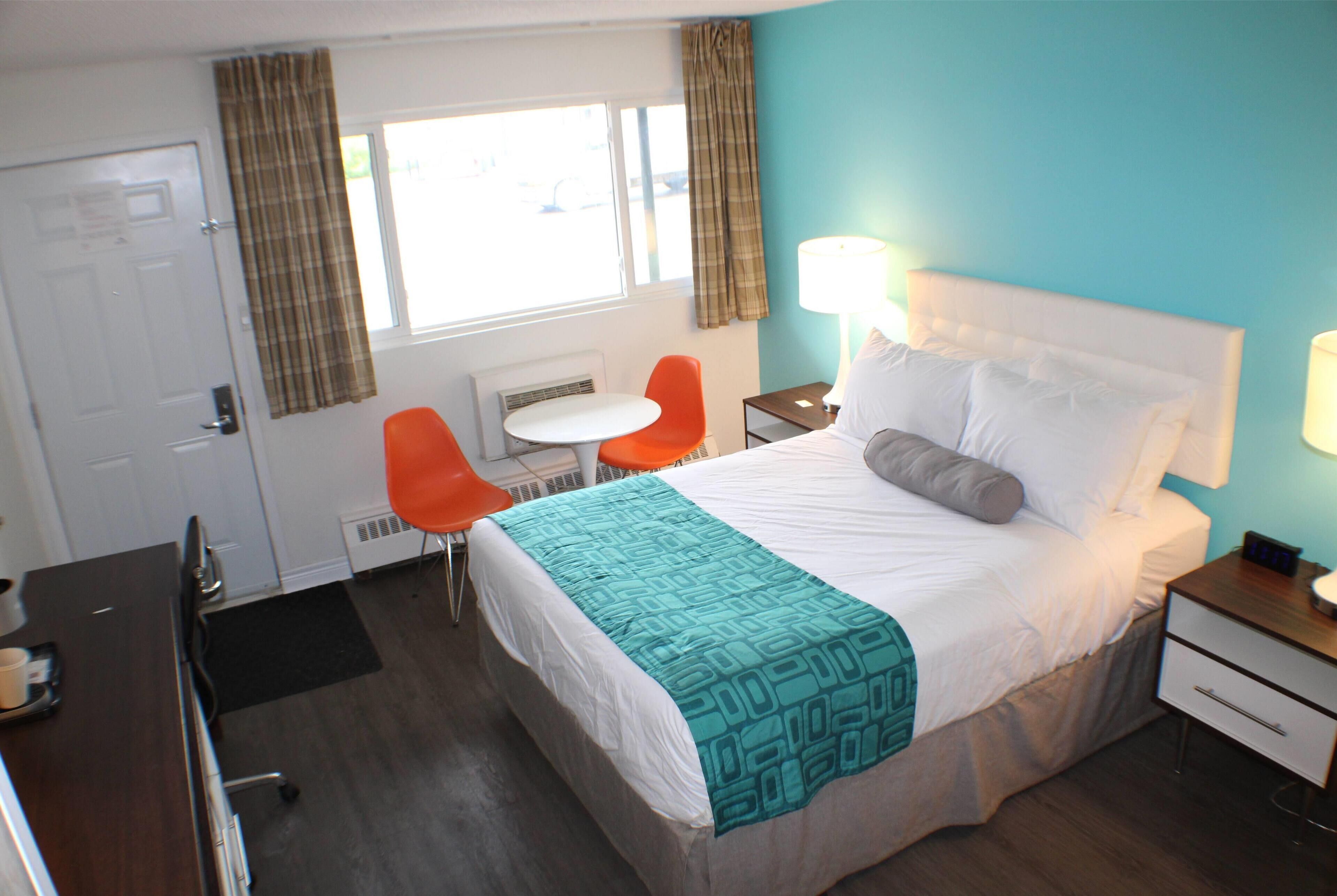 Ein Hotelzimmer mit einem Bett, einem Schreibtisch, zwei Stühlen, einem kleinen Tisch und einem Fenster mit Vorhängen.