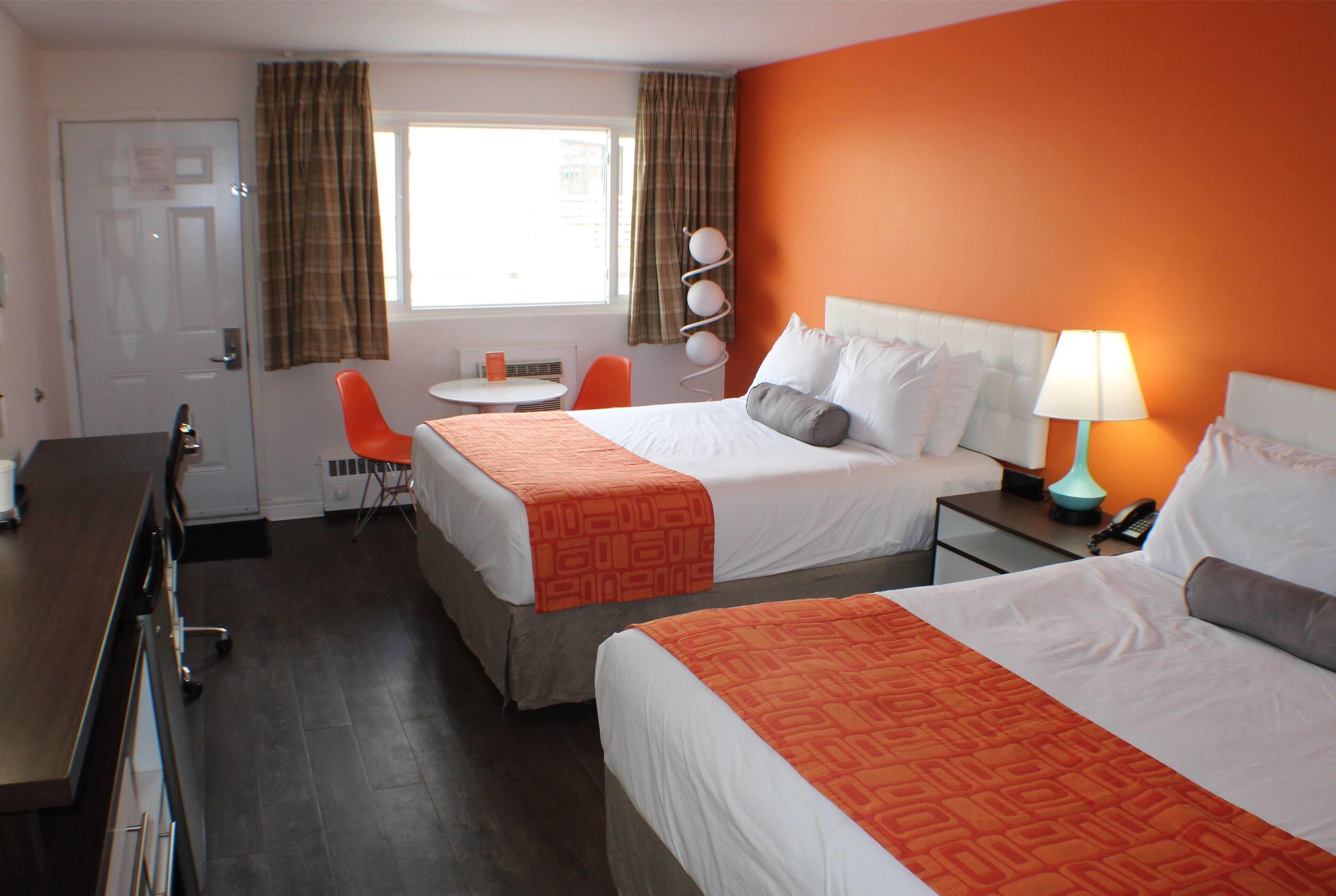 Une chambre d’hôtel avec deux lits, un bureau, une chaise, une petite table et une fenêtre avec des rideaux.