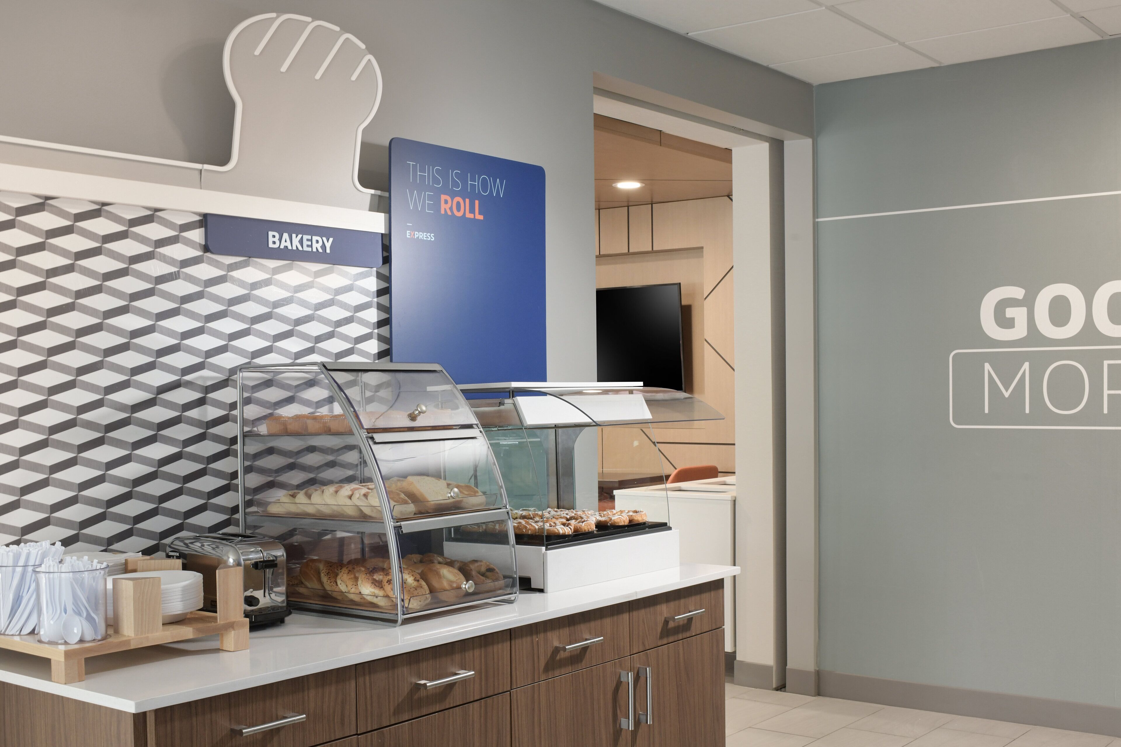 A bakery counter with a display case, a toaster, and a sign that says "THIS IS HOW WE ROLL".
