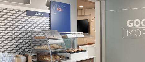 A bakery counter with a display case, a toaster, and a sign that says "THIS IS HOW WE ROLL".