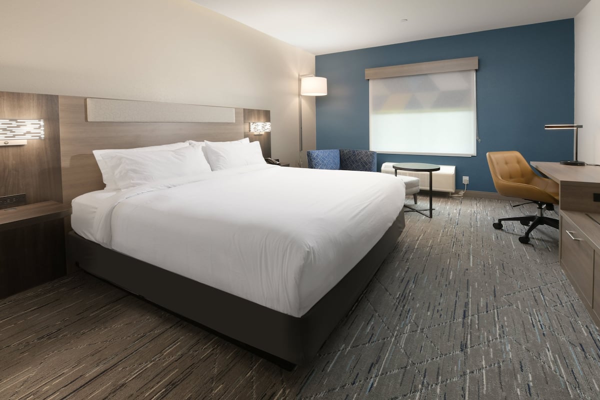 A hotel room with a large bed, a desk, a chair, and a window with blinds.