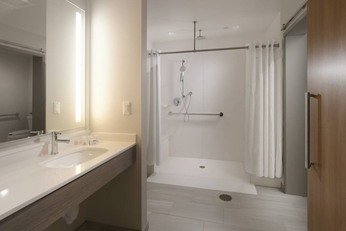 A modern bathroom with a double sink, a shower with a glass door, and a wooden door.