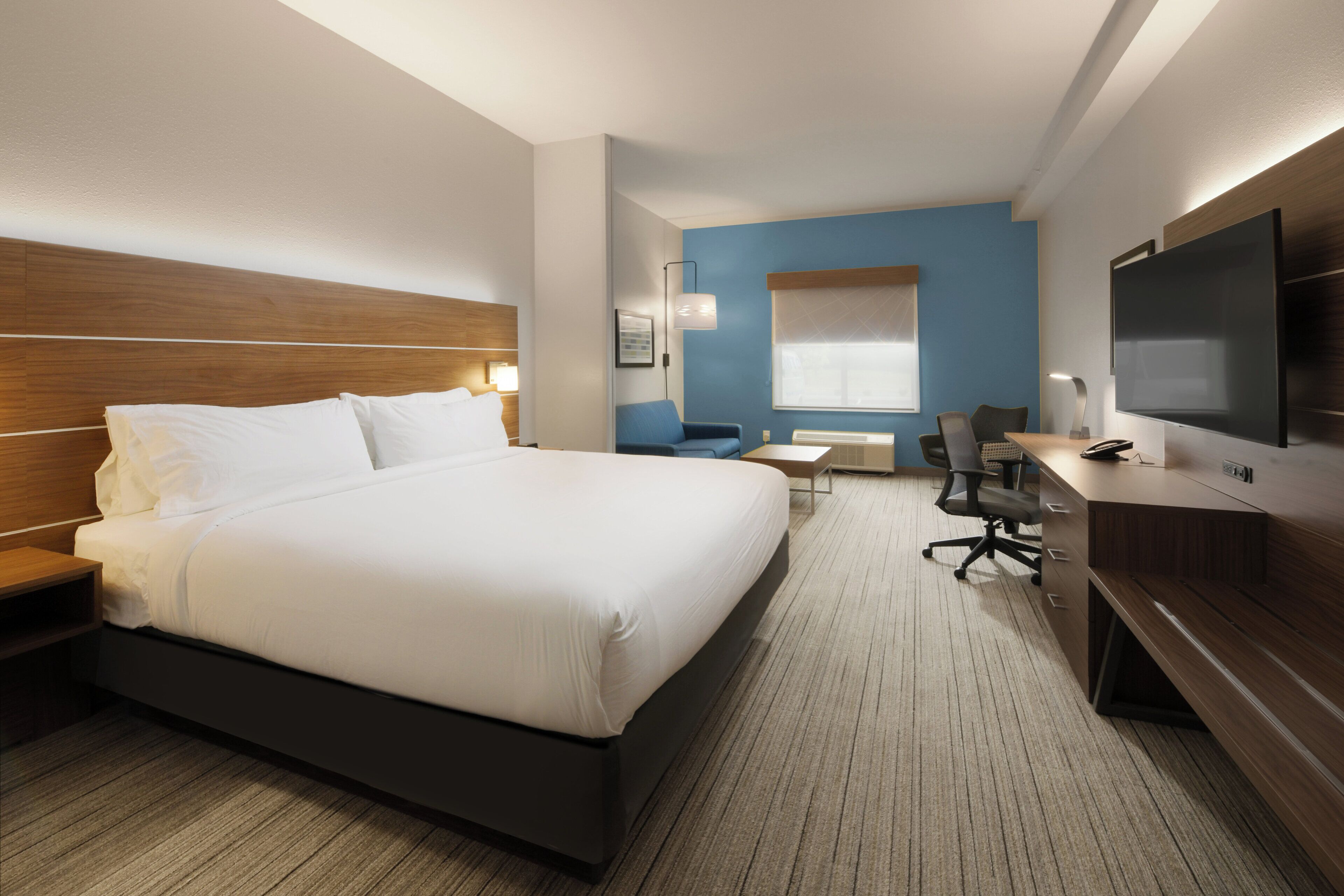 Ein Hotelzimmer mit einem großen Bett, einem Schreibtisch mit Stuhl, einem Fernseher und einem Fenster mit Jalousien.