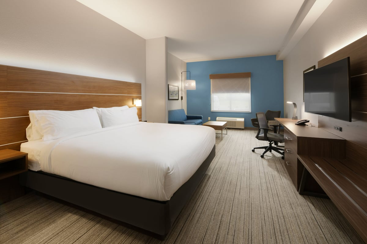 A hotel room with a large bed, a desk with a chair, a television, and a window with blinds.