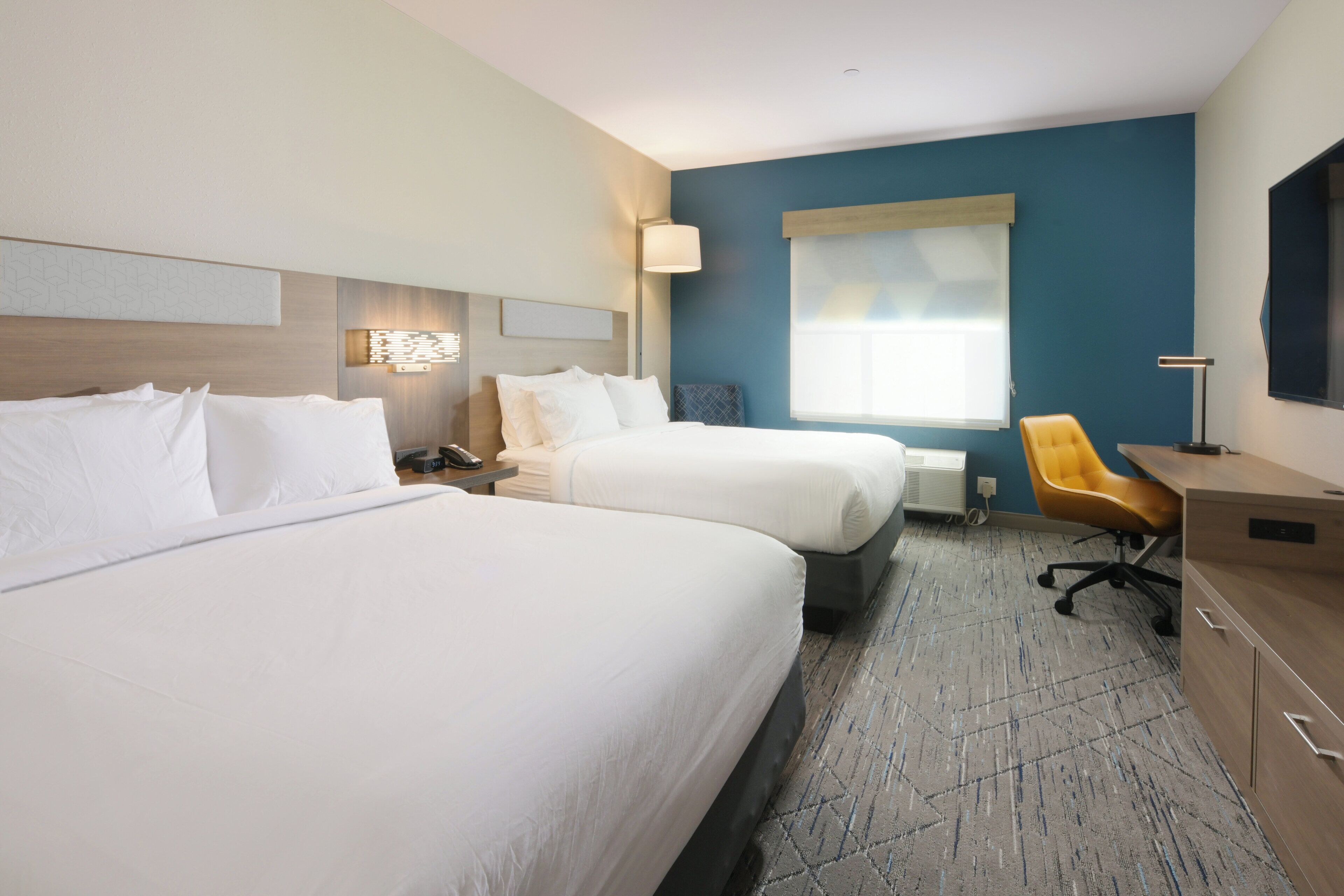 A hotel room with two beds, a desk, a chair, and a large window.