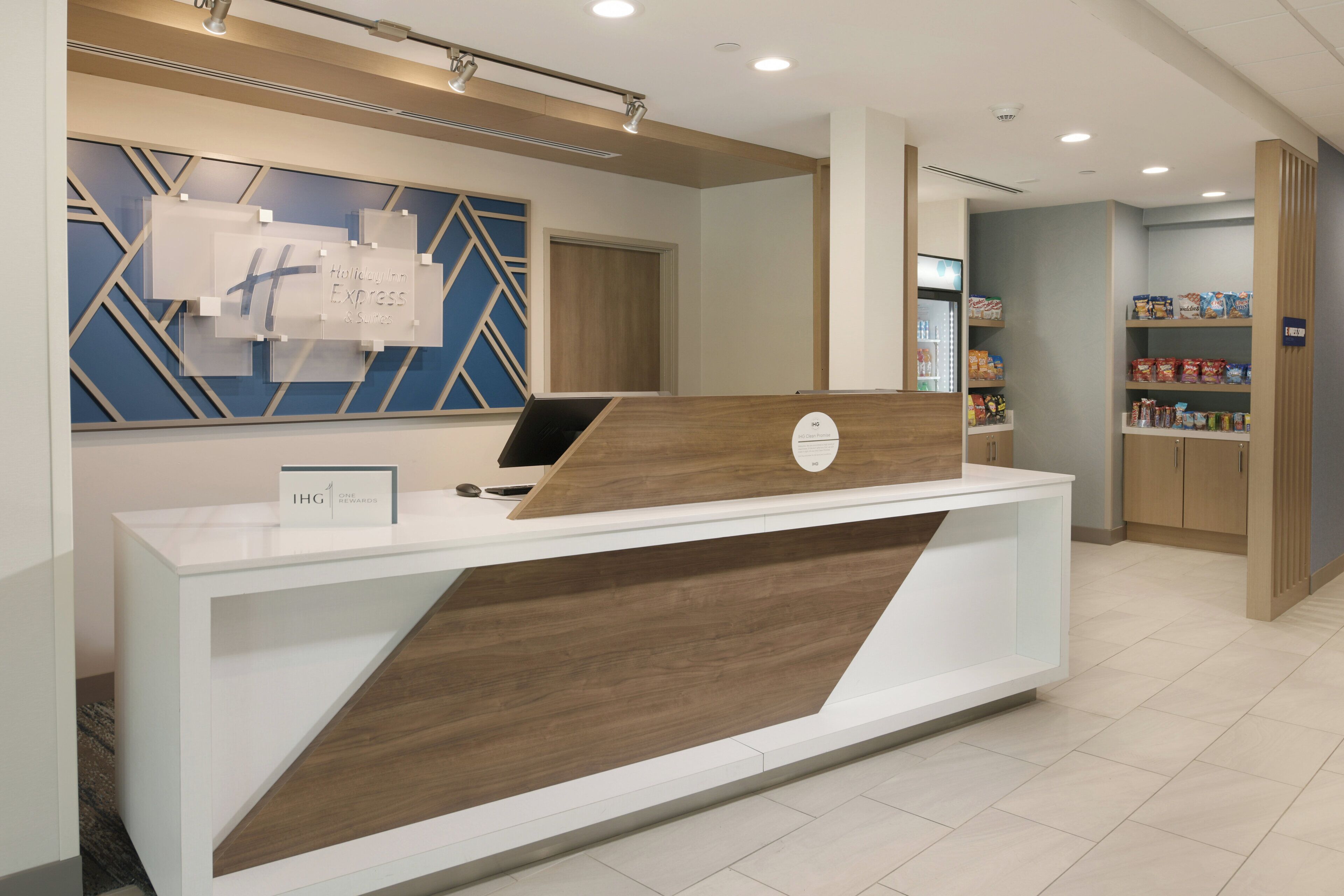 Ein moderner Hotelrezeptionsschalter, ein Schild für Holiday Inn Express & Suites und ein Bereich für Selbstbedienungskioske.
