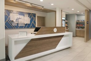 A hotel reception desk with a modern design, a sign for Holiday Inn Express & Suites, and a self-service kiosk area. - Holiday Inn Express & Suites Williamstown - Glassboro by IHG (Williamstown)