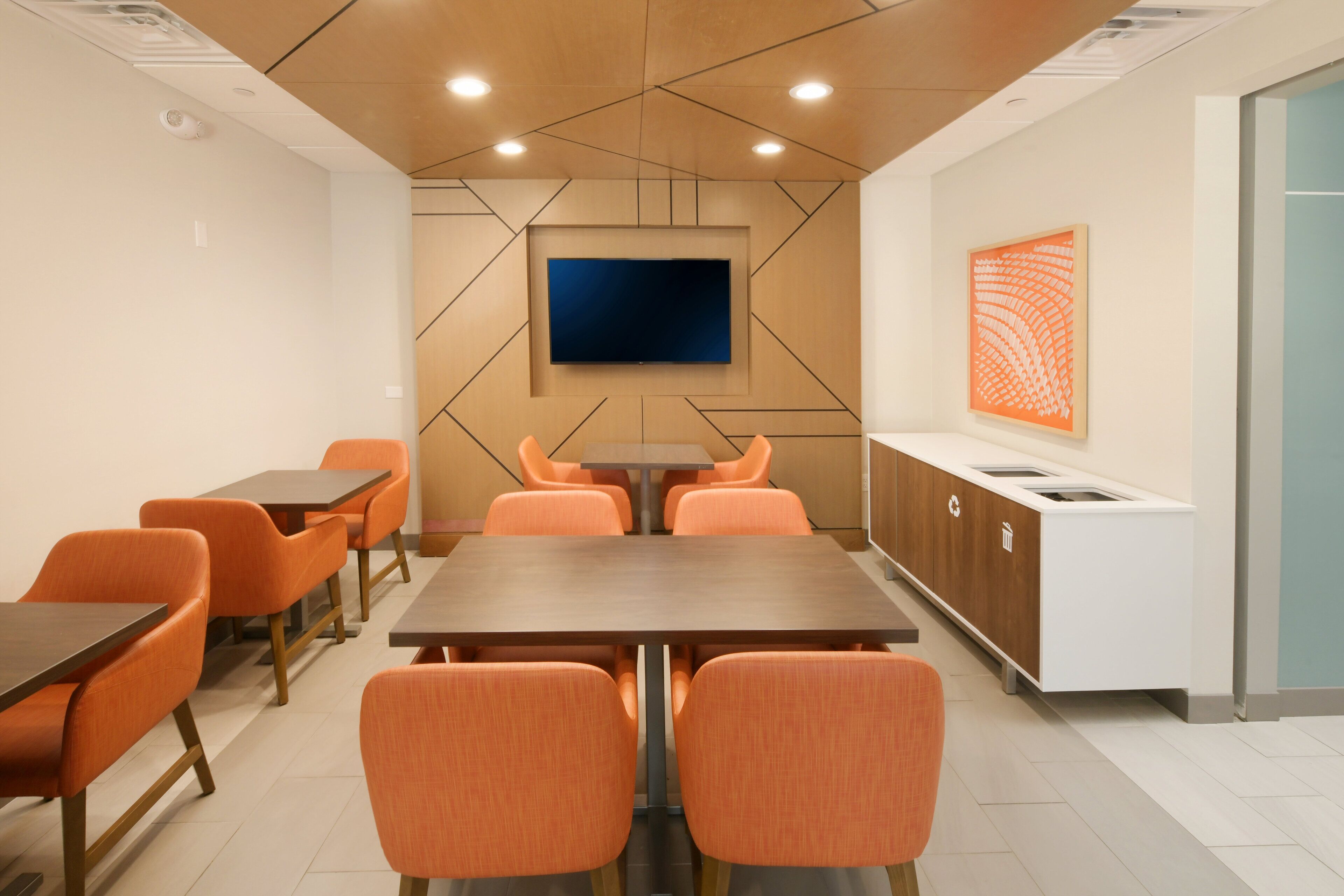 A conference room with a large table, orange chairs, a TV mounted on the wall, and a cabinet with a sink.