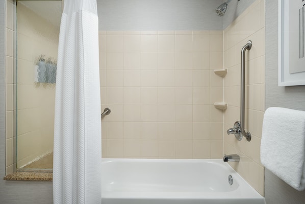 A bathroom with a bathtub, a shower area, and a handrail.