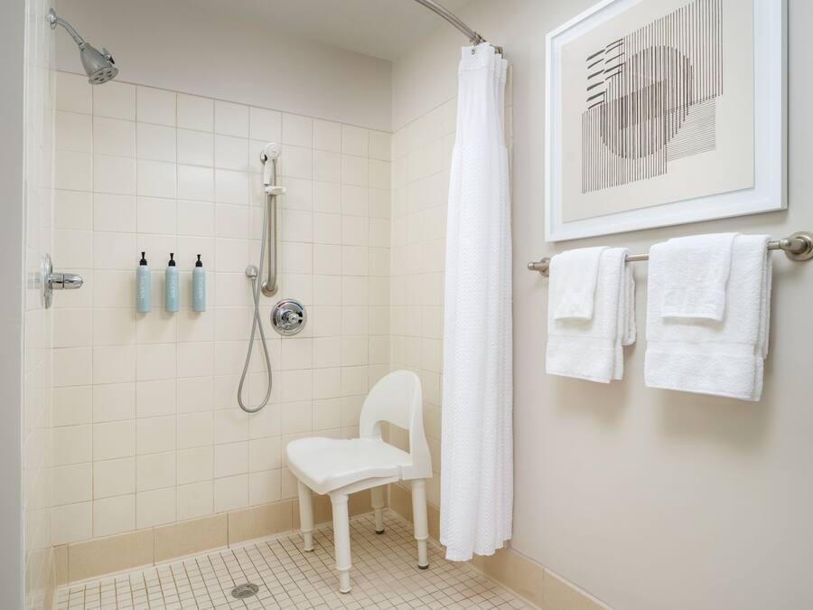 Un baño con ducha, una silla blanca y un perchero con toallas.