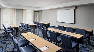 A conference room with multiple tables and chairs, a projector screen, and a patterned carpet.