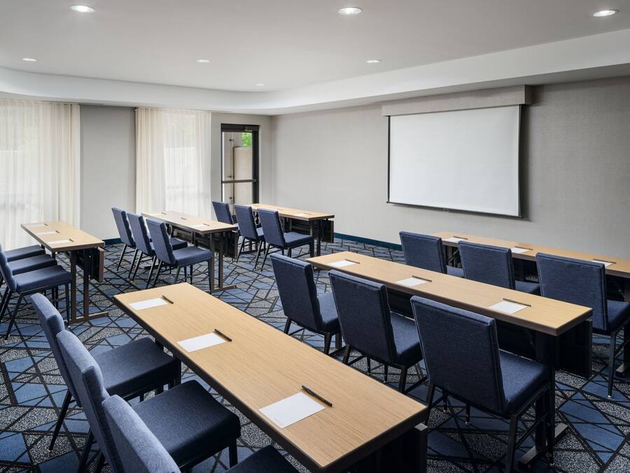 A conference room with multiple tables and chairs, a projector screen, and a patterned carpet.