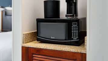 A black microwave with a coffee maker on top, placed on a granite countertop in a kitchen.