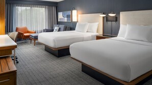 A hotel room with two beds, a desk, a chair, and a large window with curtains. - Courtyard by Marriott Kingston (Kingston)
