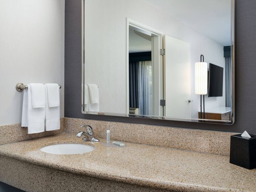 A bathroom with a granite countertop, a sink, a mirror, a towel rack, and a tissue box.
