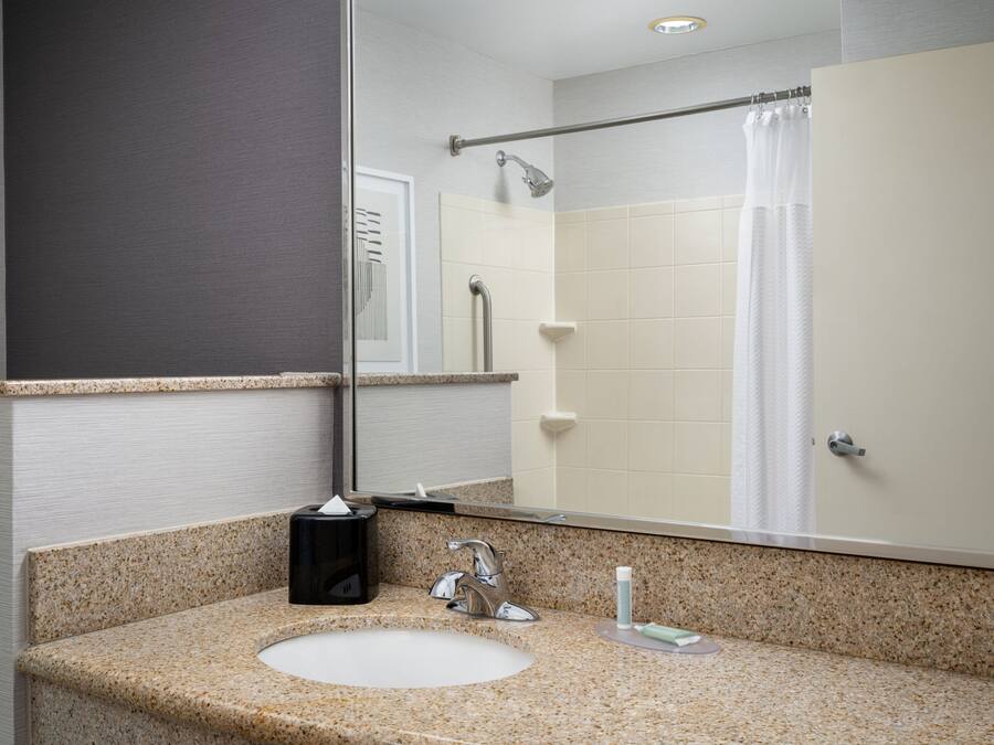 A bathroom with a granite countertop sink, a mirror, a towel rack, and a shower curtain.
