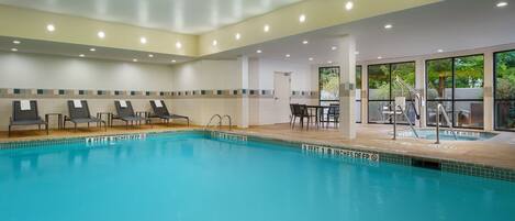 An indoor swimming pool with lounge chairs and a sunbed area.