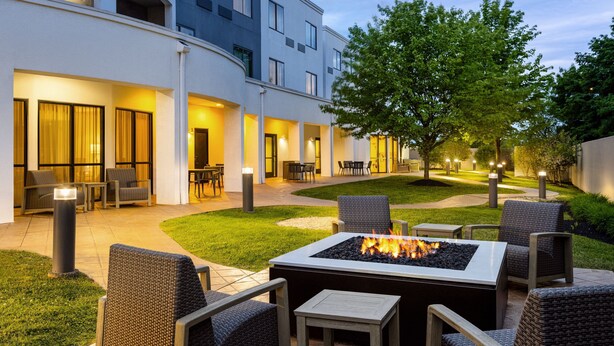 An outdoor patio with a fire pit, seating, and a building in the background. - Courtyard by Marriott Kingston (Kingston)