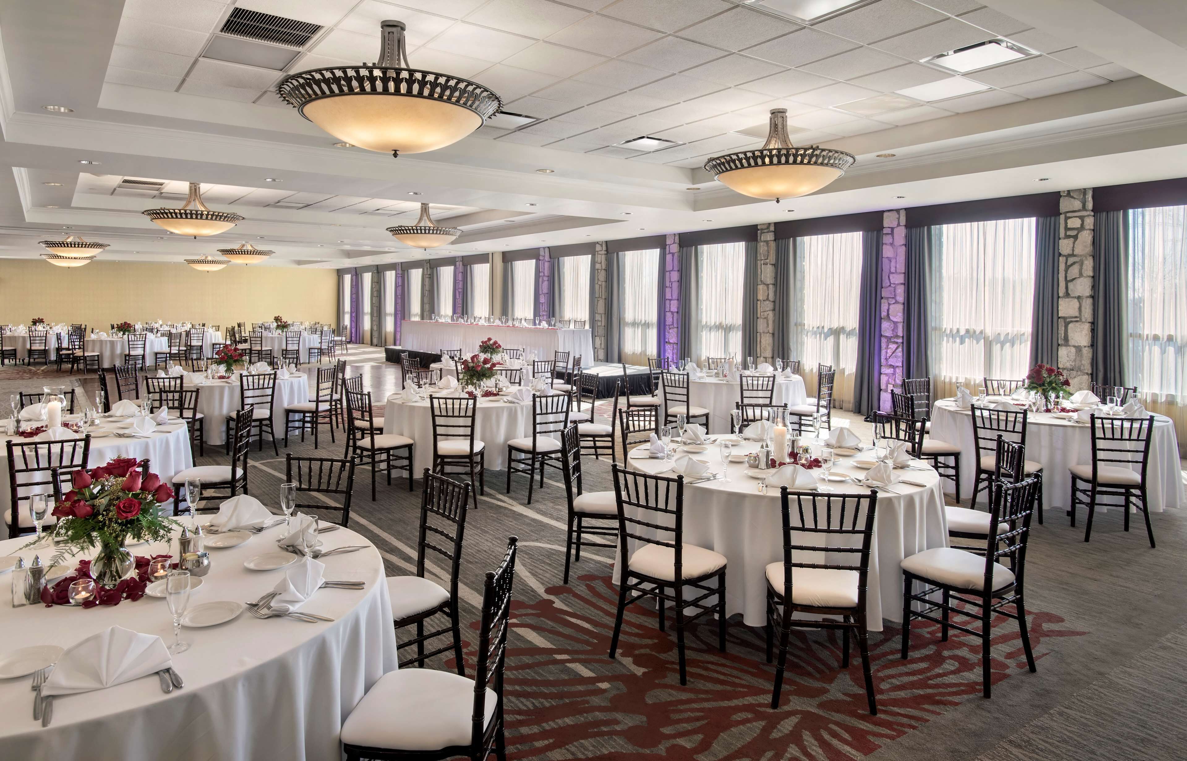 A banquet hall with multiple round tables, each set with white tablecloths, chairs, and centerpieces.