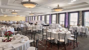A banquet hall with multiple round tables, each set with white tablecloths, chairs, and centerpieces.