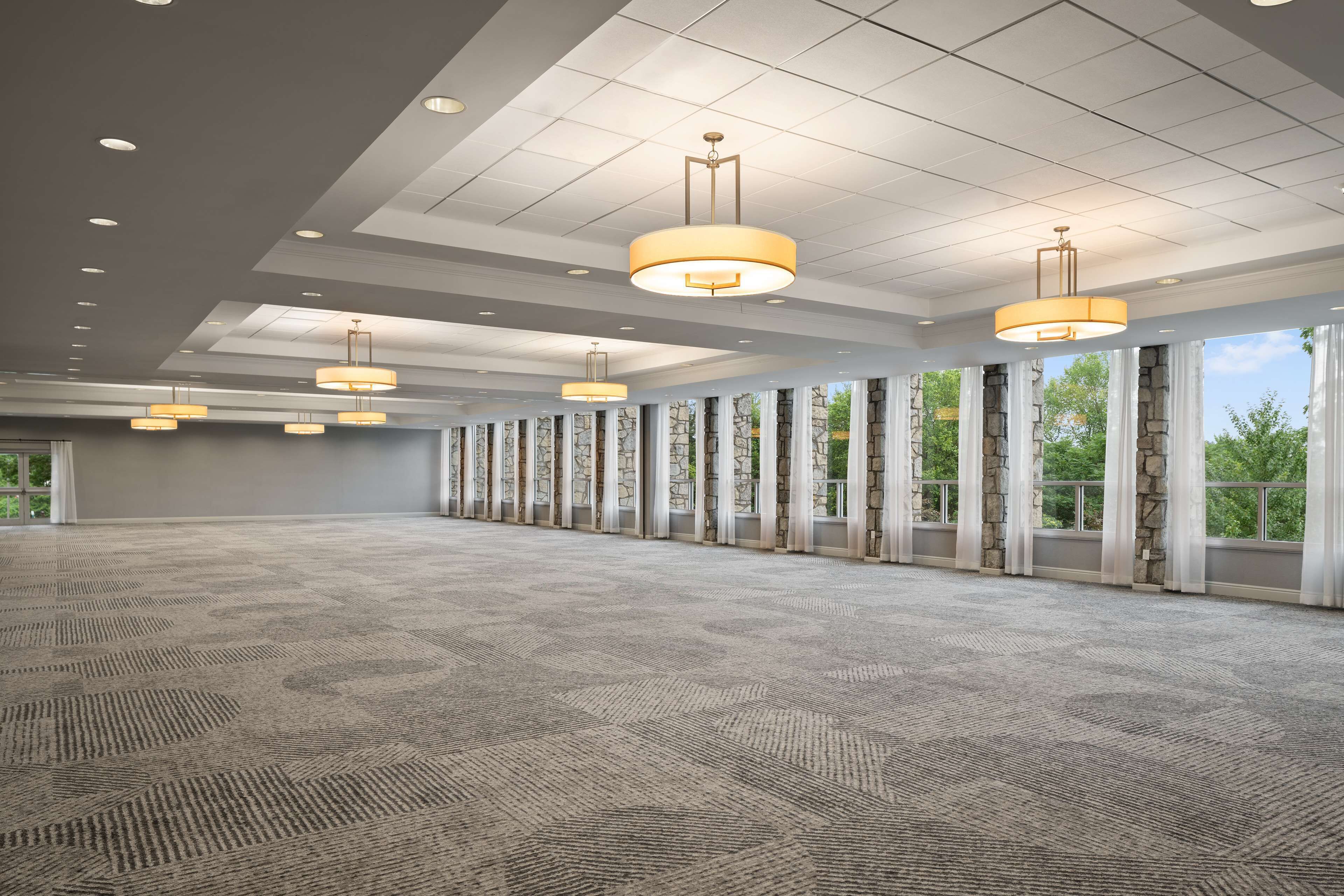 A spacious conference room with a patterned carpet, large windows with stone frames, and multiple hanging pendant lights.