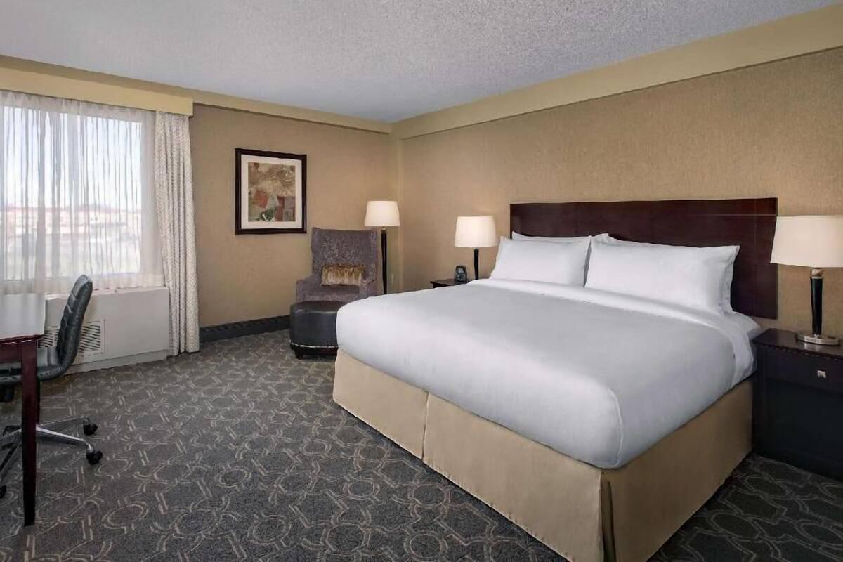 A hotel room with a large bed, a desk, a chair, and a window with curtains.