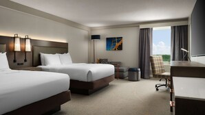 A hotel room with two beds, a desk, a chair, a trash bin, a lamp, and a painting on the wall. - DoubleTree by Hilton Pittsburgh Airport (Coraopolis)