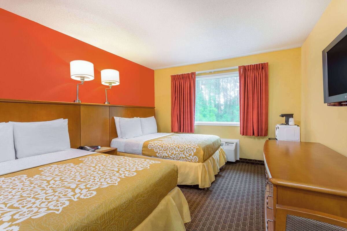 A hotel room with two beds, a wooden headboard, a television, and a window with curtains.