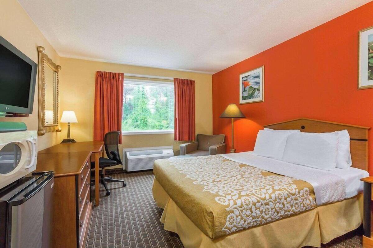 A hotel room with a bed, desk, chair, television, and a window with curtains.