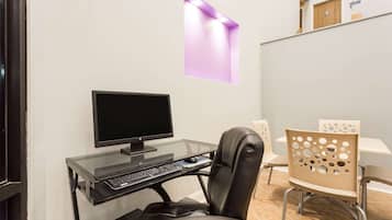 A modern office space with a glass desk, a black monitor, a keyboard, and a leather chair. There is a white table with a unique perforated design and a wooden door in the background.