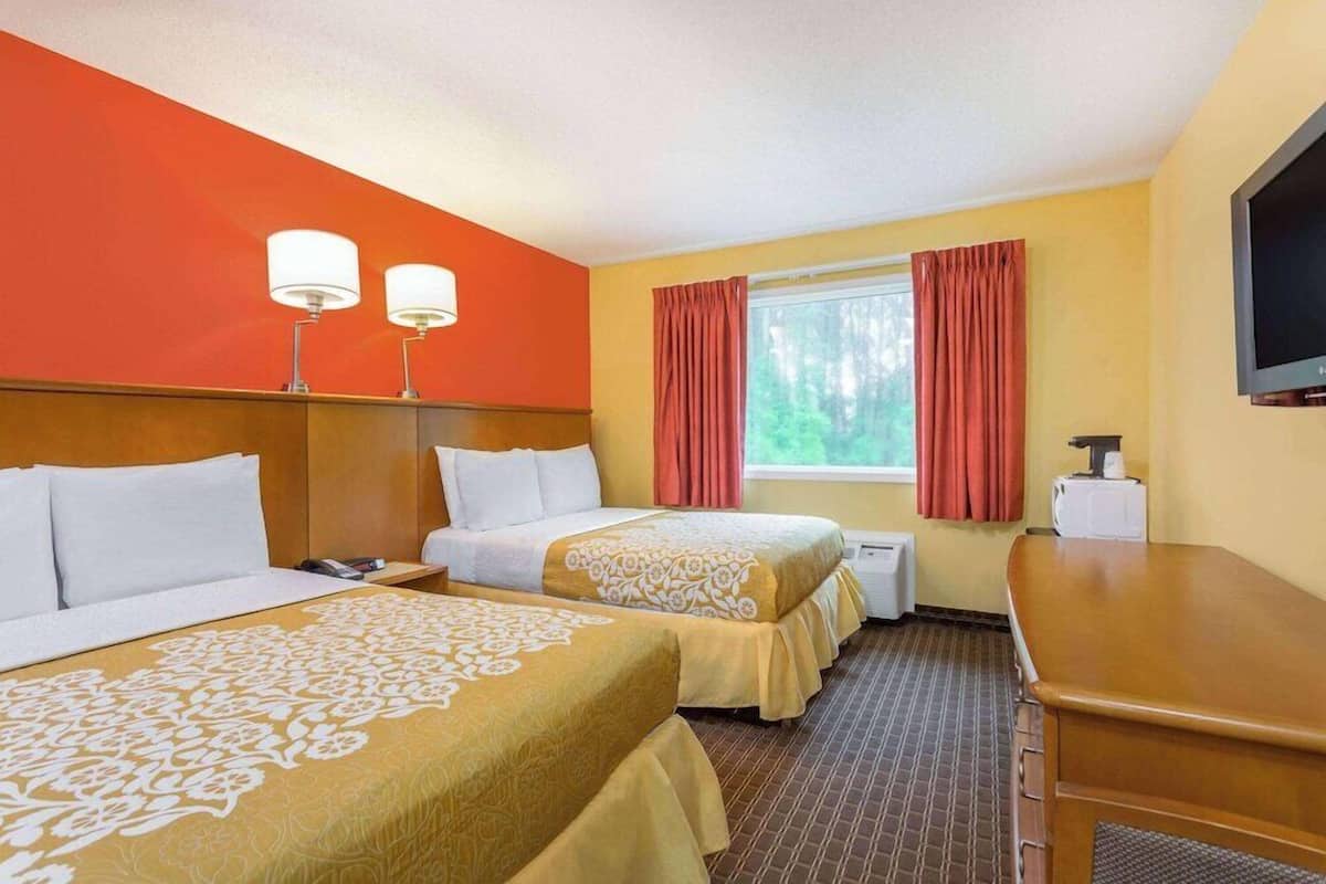 A hotel room with two beds, a desk, a TV, and a window with curtains.