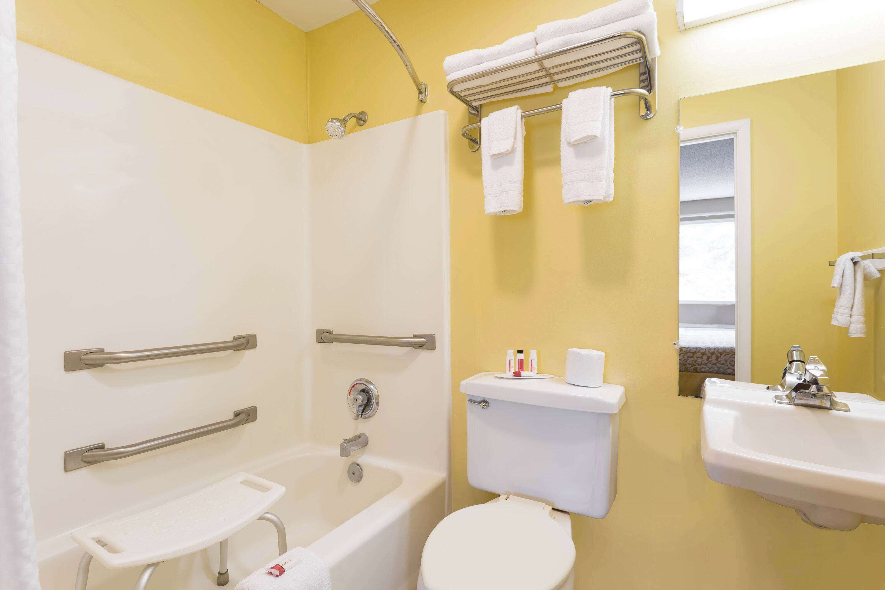 A bathroom with a bathtub, toilet, and sink, equipped with grab bars and a shower chair.
