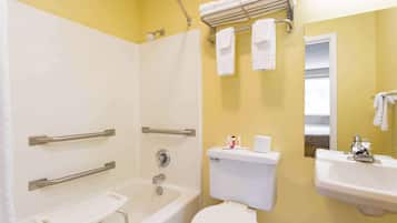 Et badeværelse med badekar, toilet og håndvask, udstyret med gelændere og en brugestol.