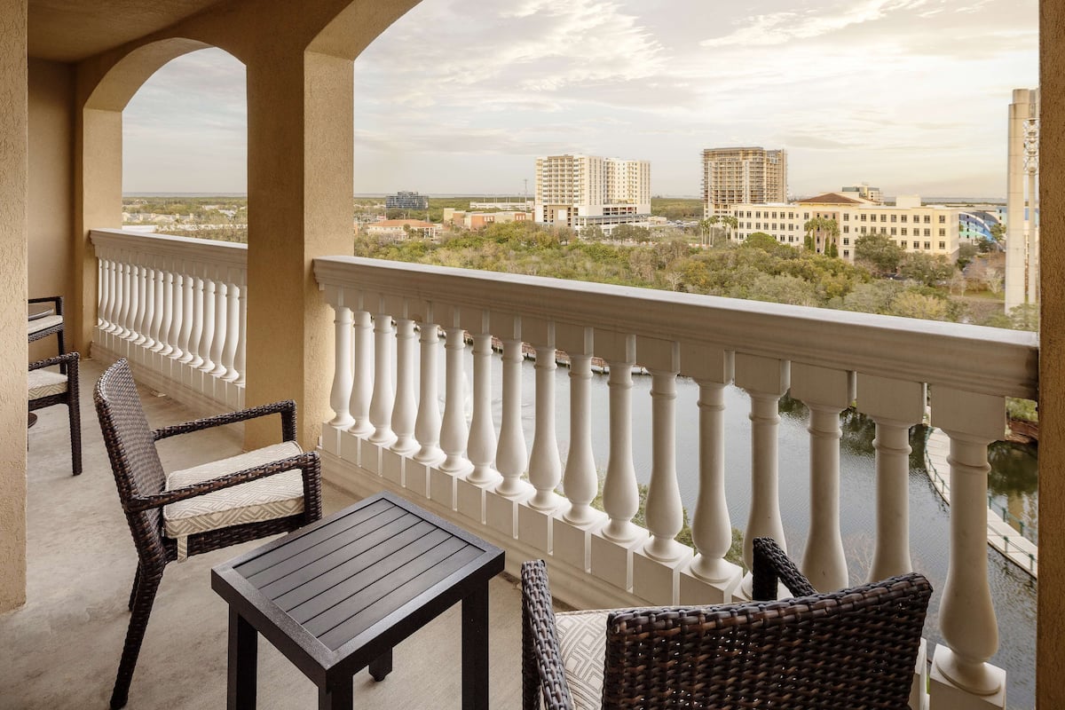 A balcony with wicker furniture, a view of a river, and buildings in the background.