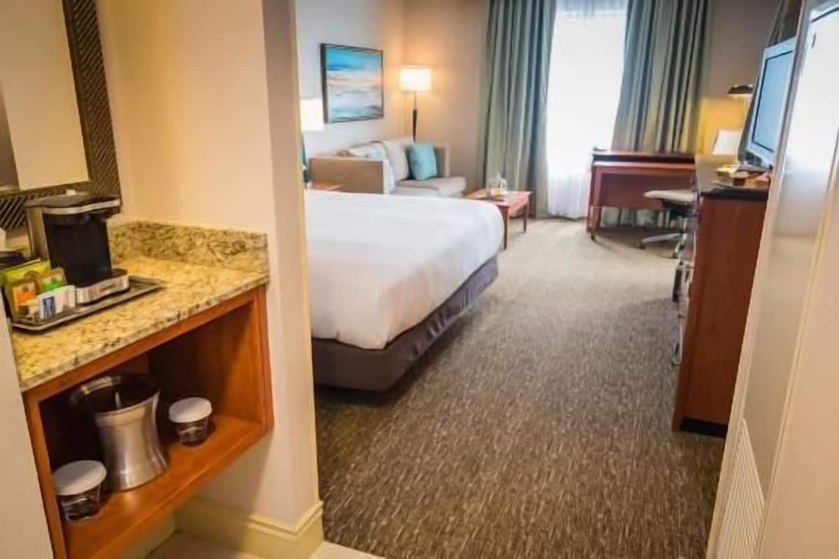 A hotel room with a bed, a desk, a chair, a TV, a coffee maker, and a painting on the wall.