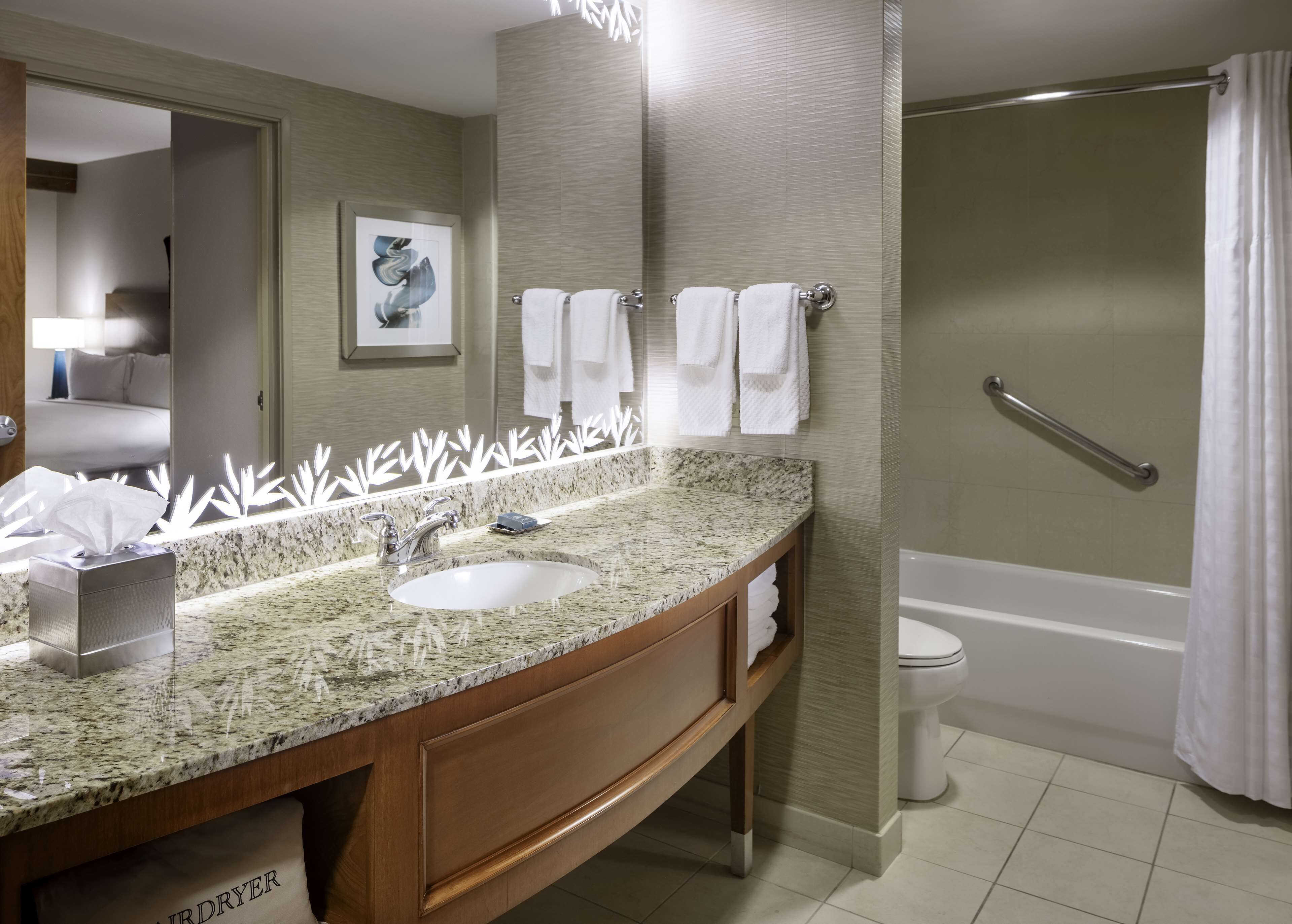 Baño con lavamanos de encimera de granito, un espejo y zona de ducha.