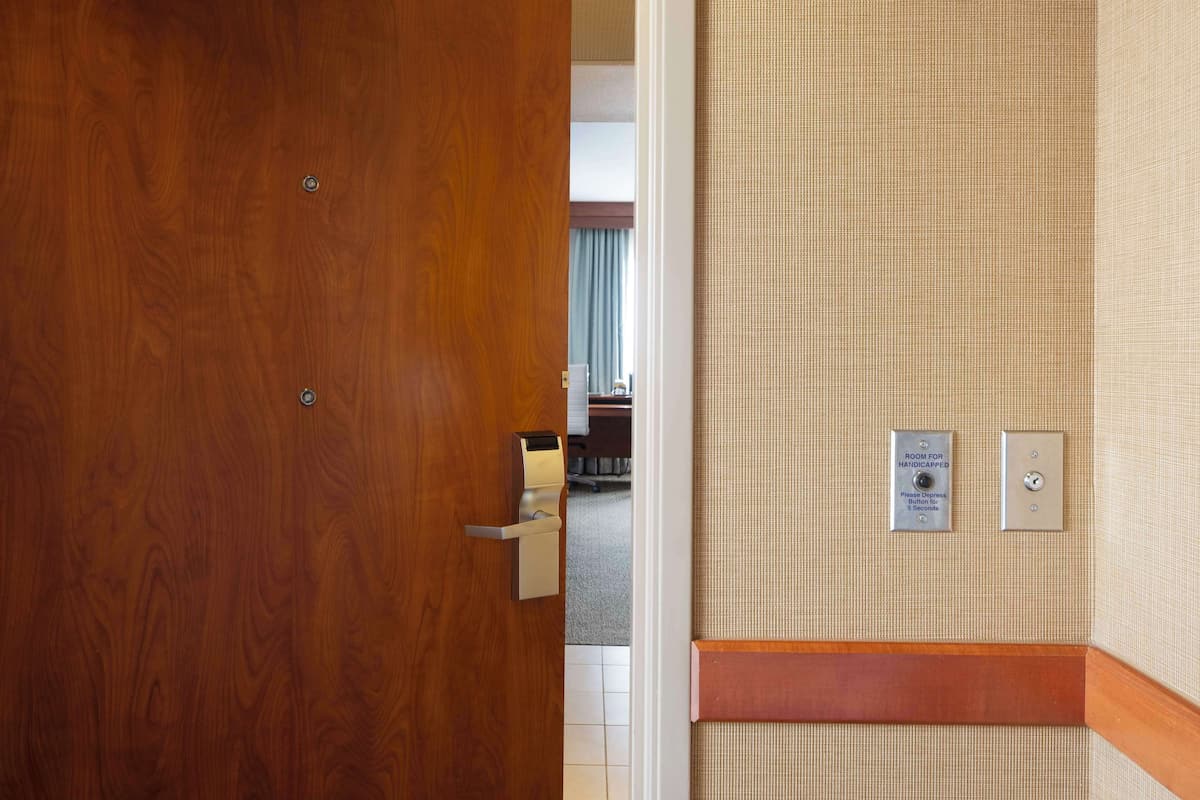 A hotel room with a wooden door, a wall-mounted sign indicating a room for the handicapped, and a small button for assistance.