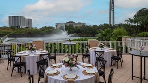 A rooftop dining area with round tables set for a meal, overlooking a body of water and a cityscape. - Hilton St. Petersburg Carillon Park (St. Petersburg)