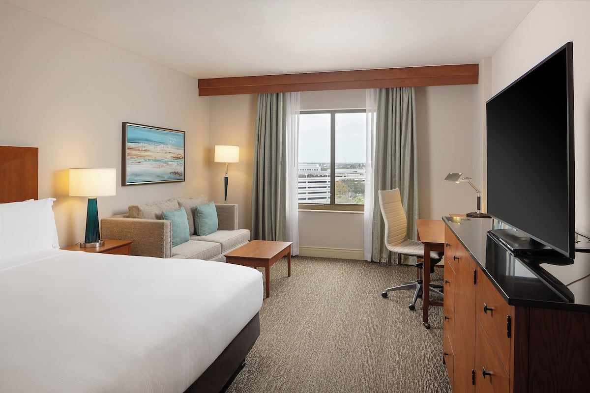 A hotel room with a large bed, a desk, a chair, a television, and a window with curtains.